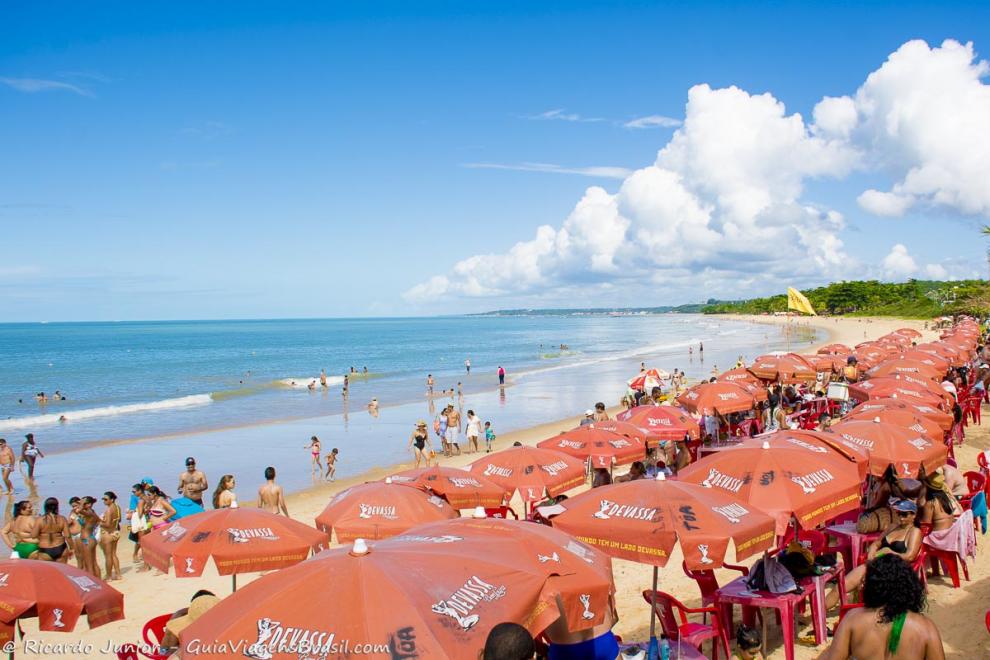 Imagem de um pedaço da Praia de Taperapuan repleta de guarda sol e turistas.